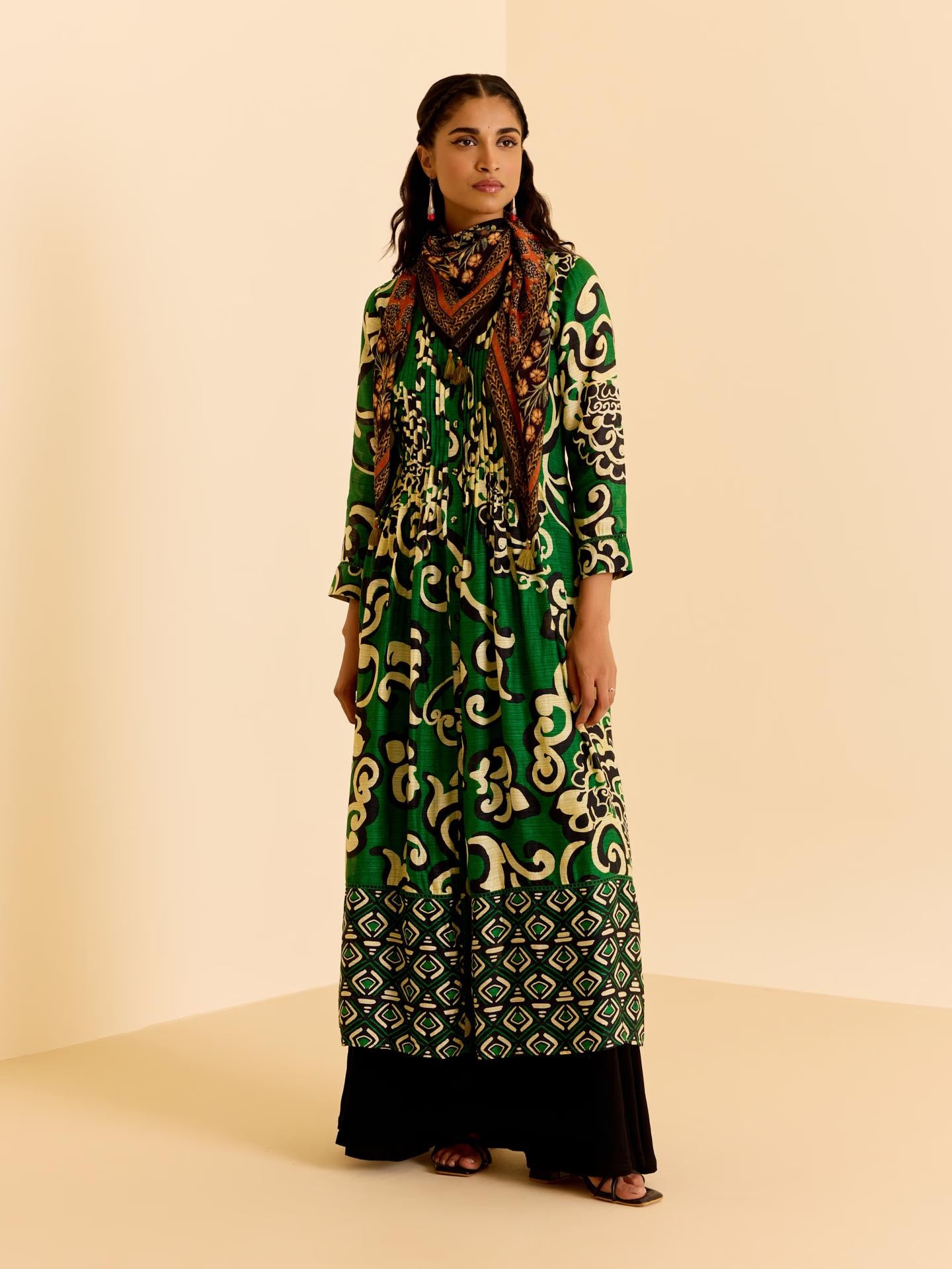 Woman wearing a green patterned dress and scarf on a beige background