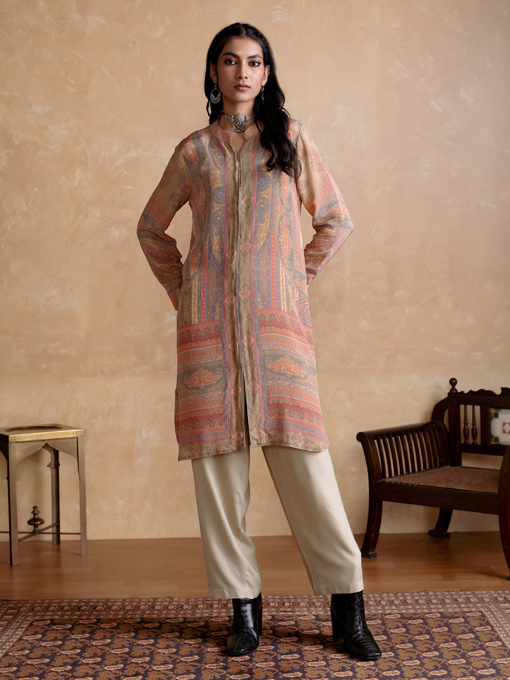 Woman wearing a patterned kurta with beige pants in a room with a wooden bench and small table.