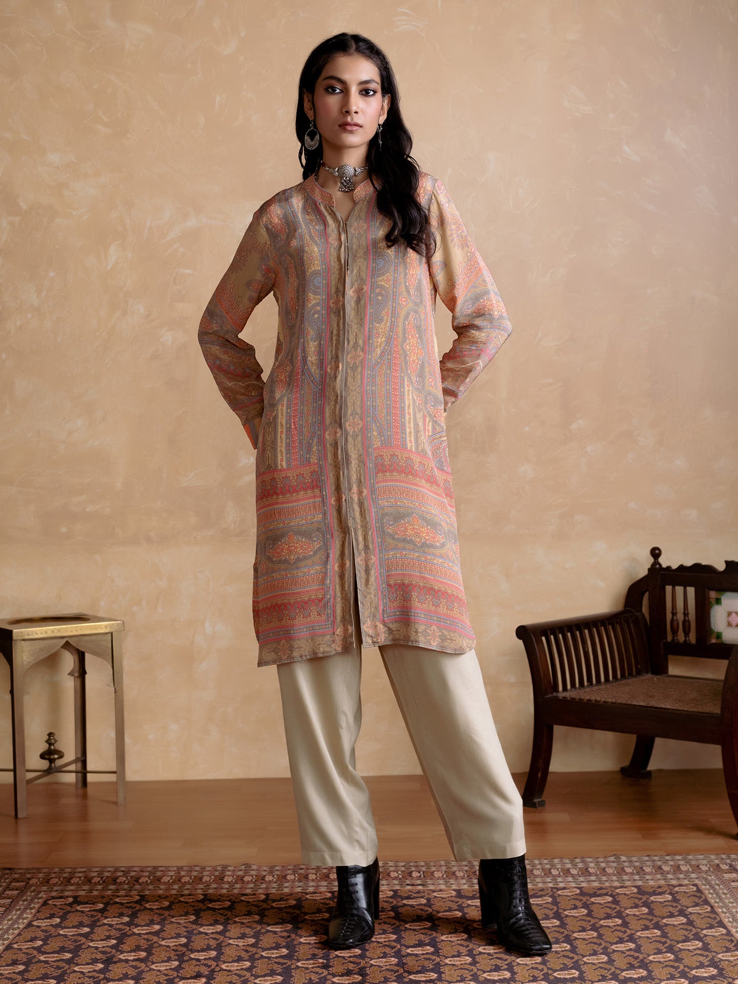 Woman wearing a patterned kurta with beige pants in a room with a wooden bench and small table.