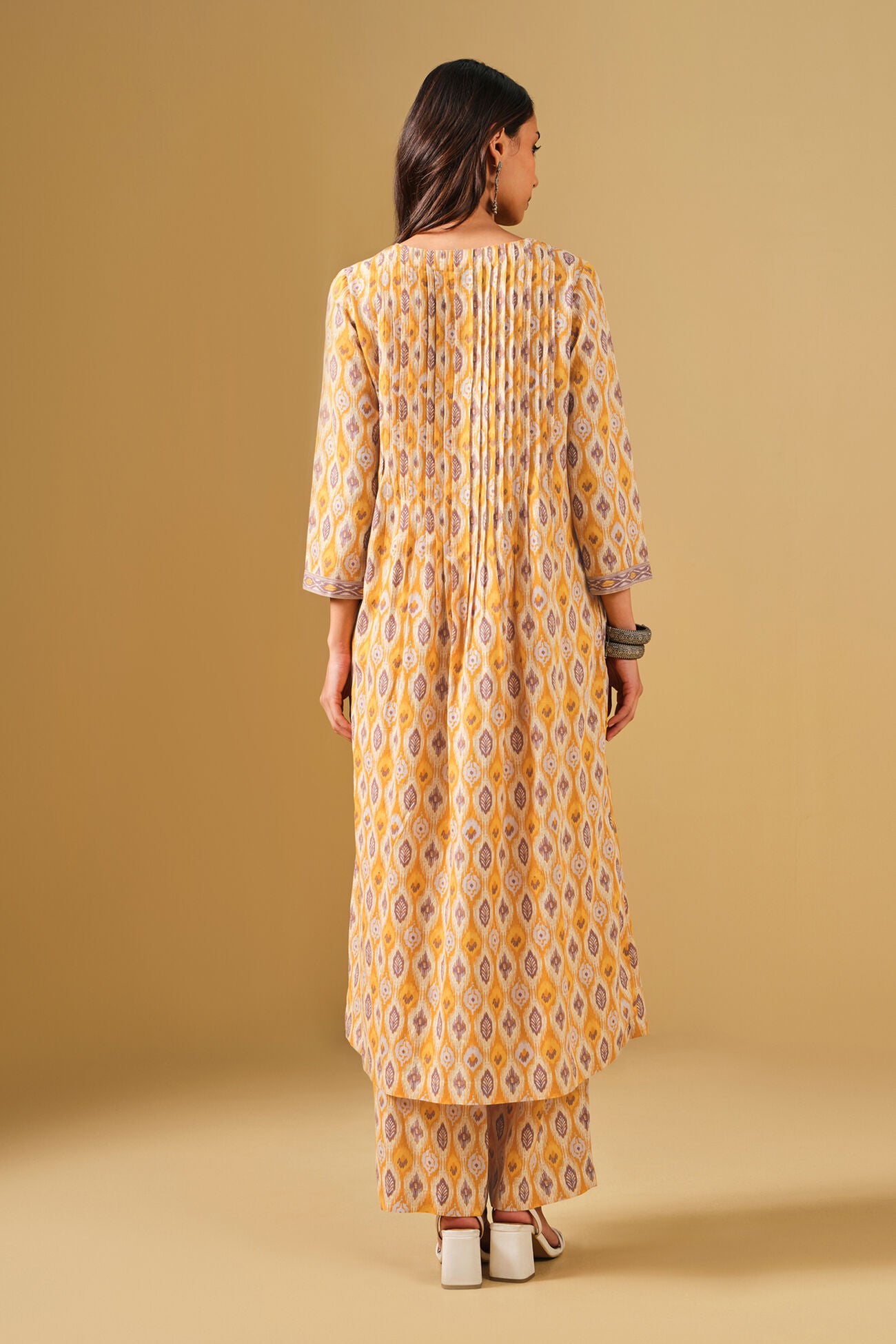 Woman wearing a yellow patterned kurta with pants on a beige background