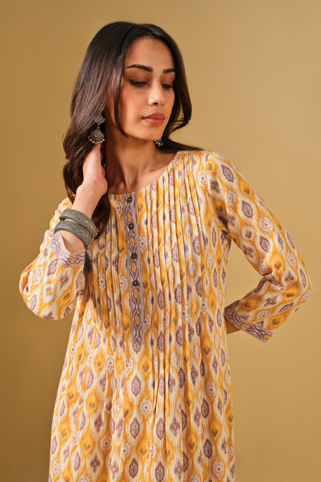 Woman wearing a yellow patterned dress against a beige background