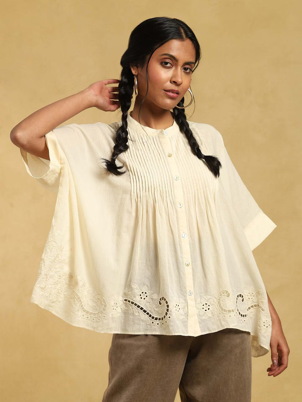 Woman wearing a cream-colored blouse with intricate designs on a beige background