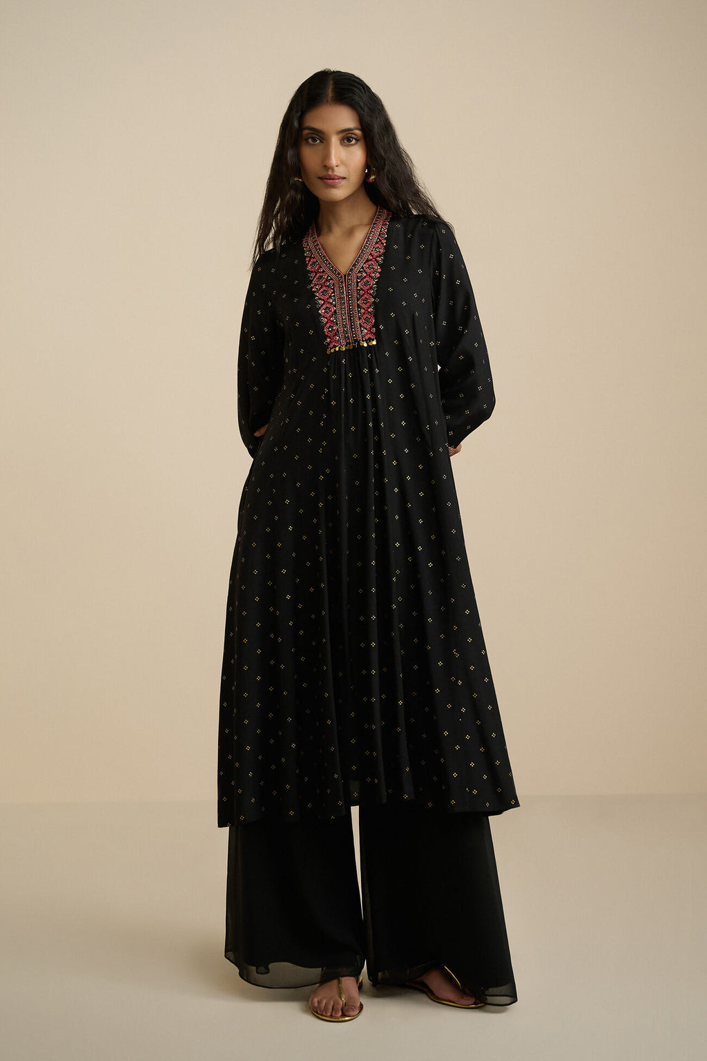 Woman wearing a black traditional outfit with intricate embroidery on a beige background