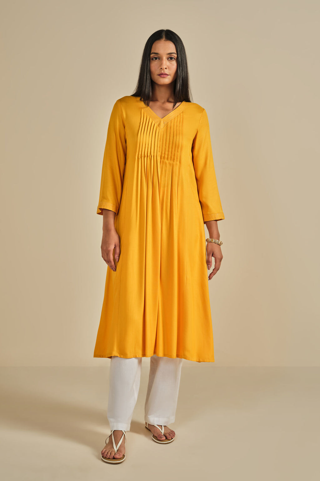 Woman wearing a yellow kurta with white pants on a beige background