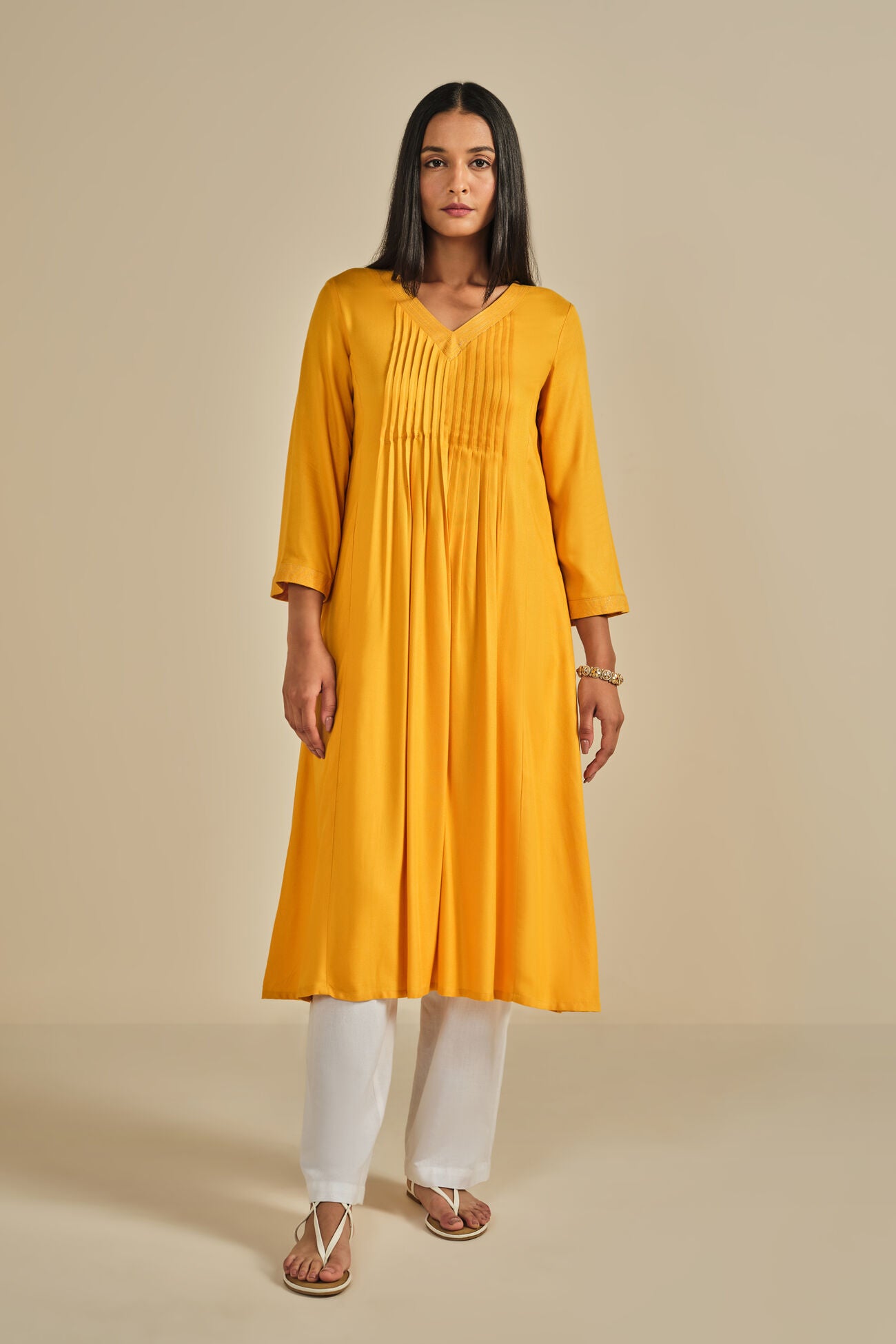 Woman wearing a yellow kurta with white pants on a beige background