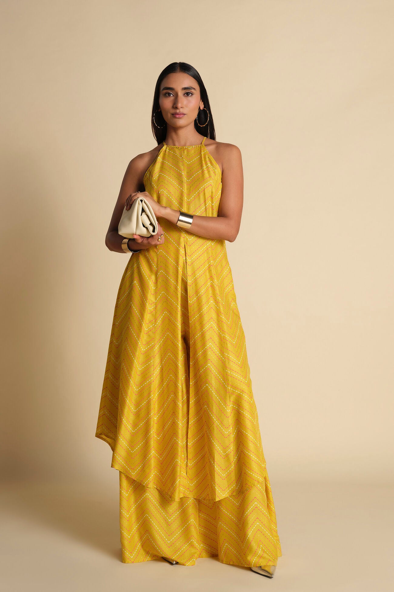 Woman wearing a yellow dress holding a clutch against a beige background