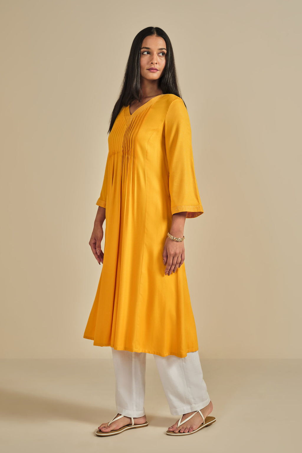 Woman wearing a yellow kurta with white pants on a beige background