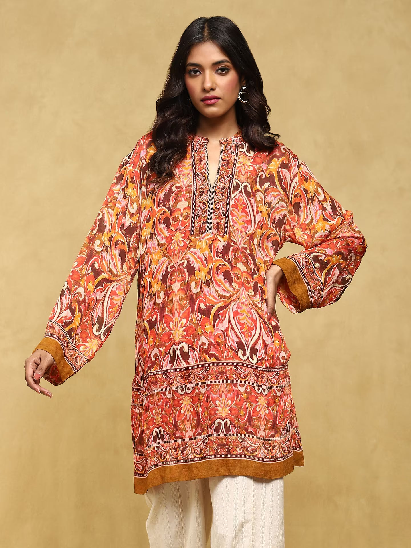 Woman wearing a patterned orange and brown dress against a beige background