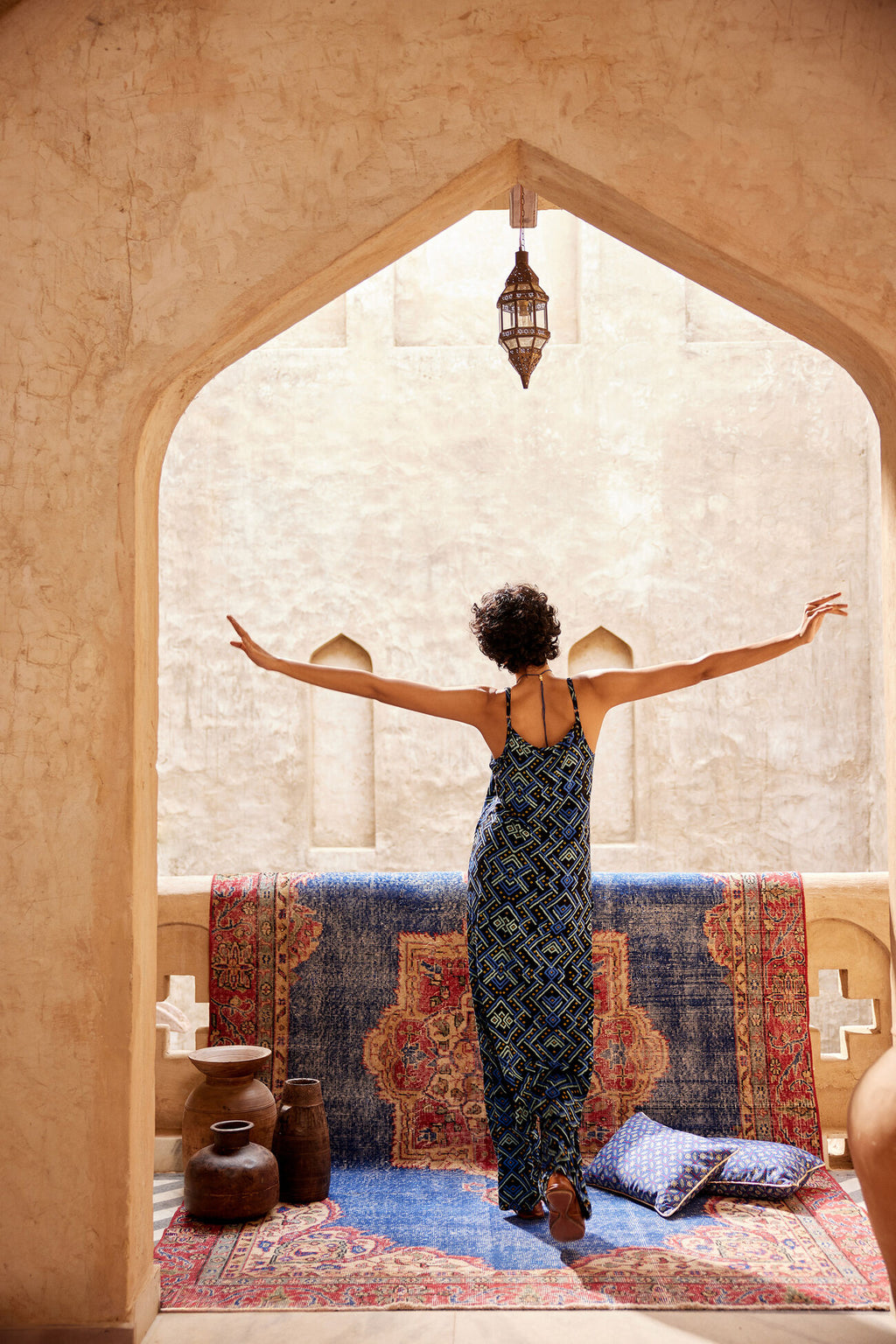 Woman standing with arms outstretched in a room with a colorful rug and decorative pillows.