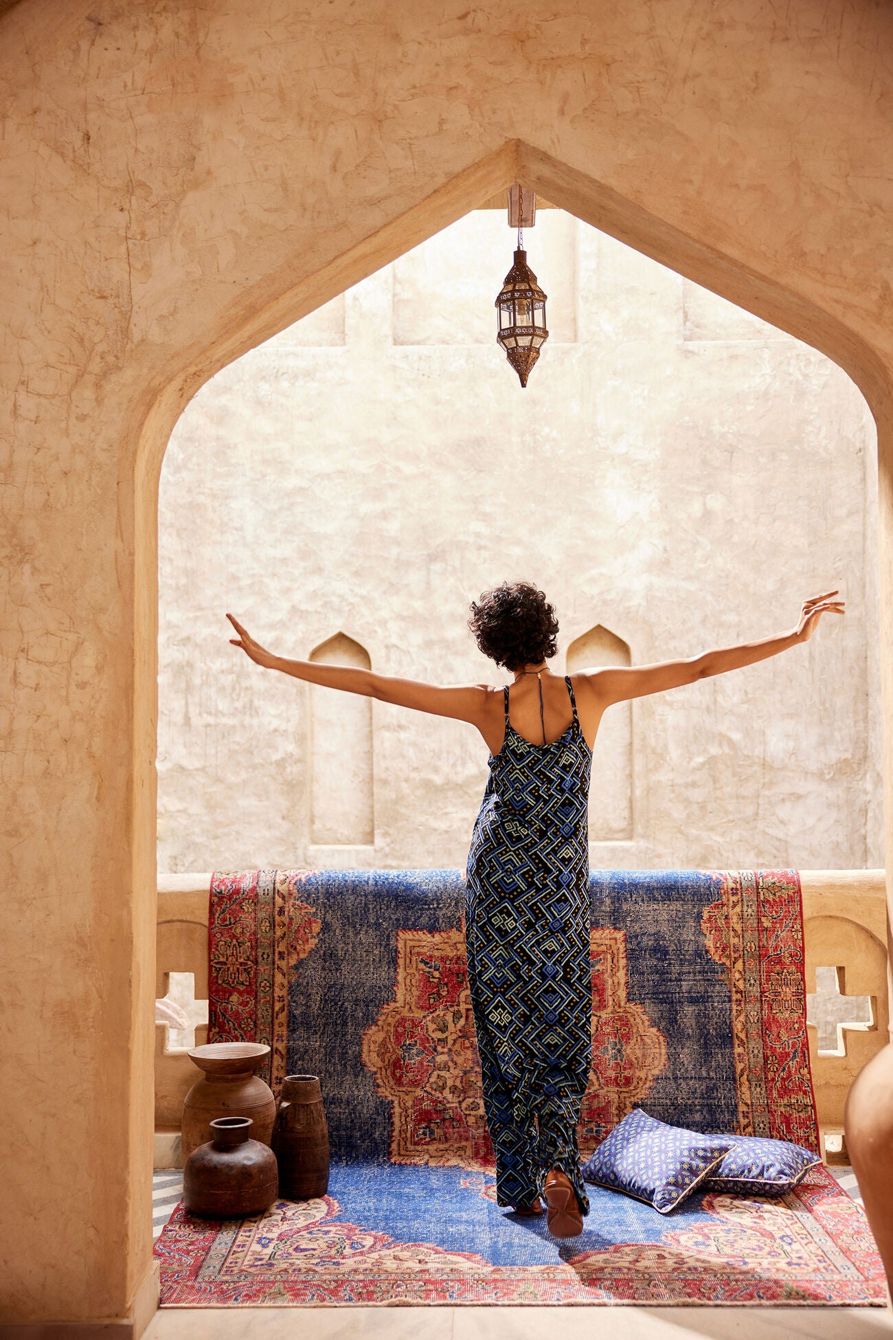 Woman standing with arms outstretched in a room with a colorful rug and decorative pillows.