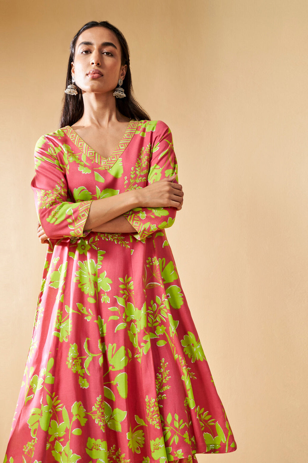Woman wearing a pink dress with green floral patterns against a beige background