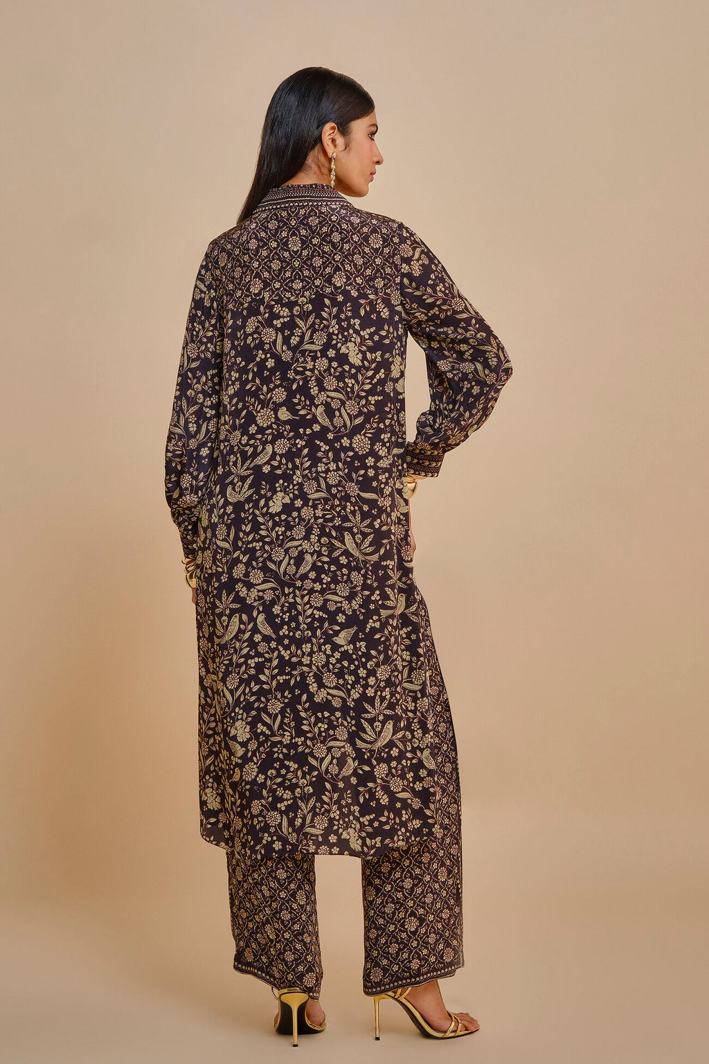 Woman wearing a long, dark floral-patterned dress against a beige background