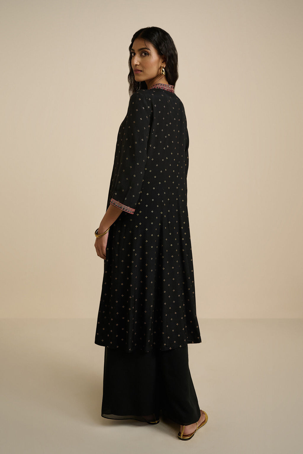 Woman wearing a black patterned kurta with palazzo pants on a beige background