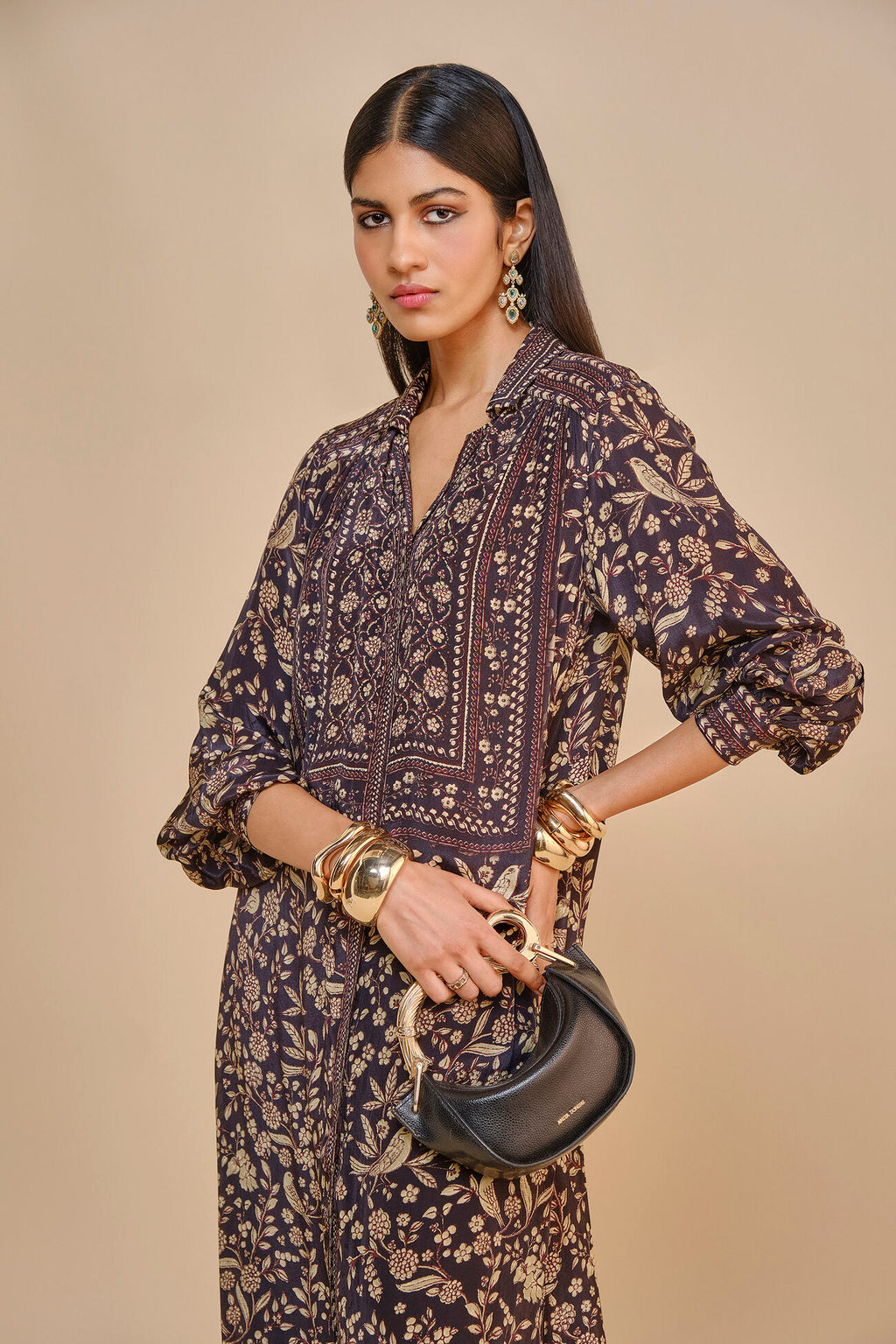 Woman wearing a patterned dress holding a handbag against a beige background