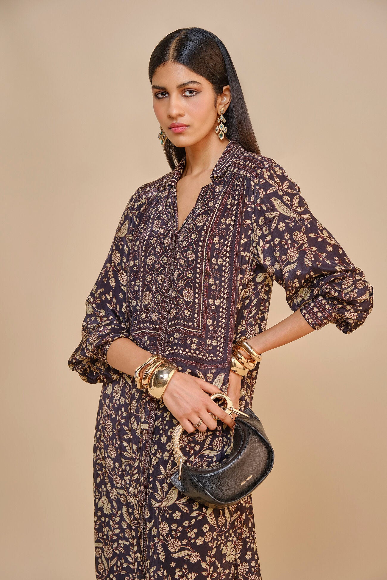 Woman wearing a patterned dress holding a handbag against a beige background