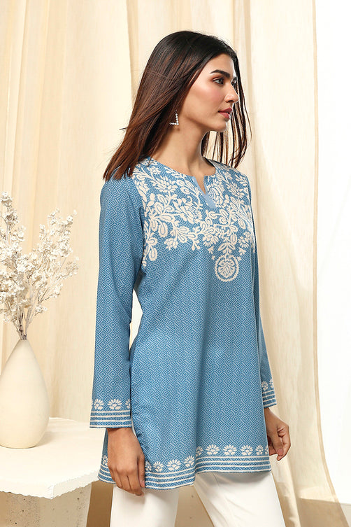 Woman wearing a blue embroidered kurta with white pants against a beige curtain background