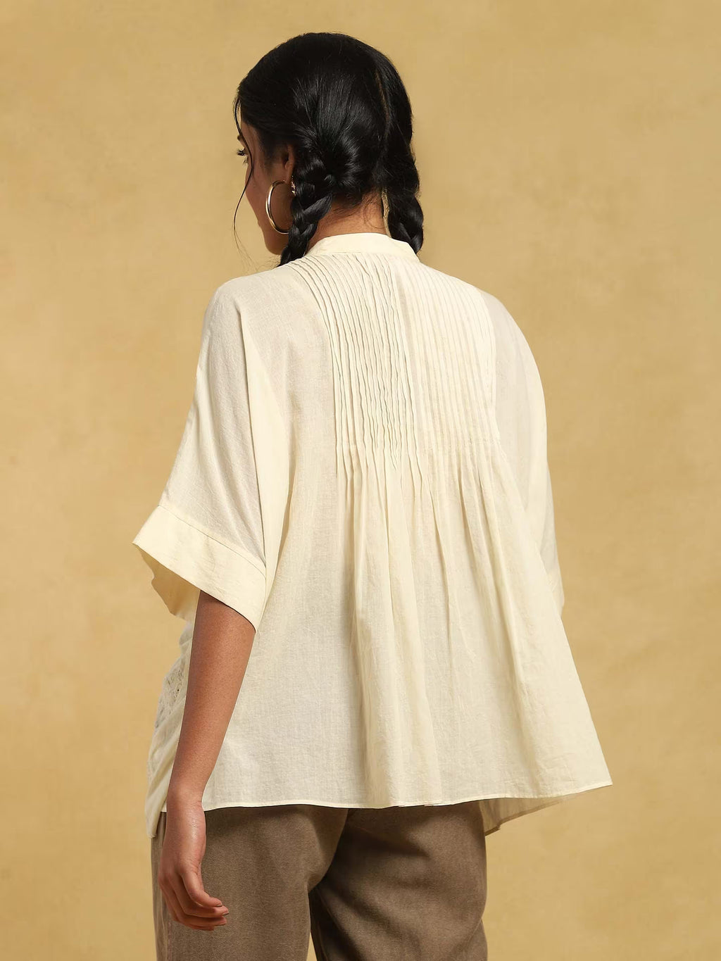 Woman wearing a beige kurta top and brown pants against a beige background