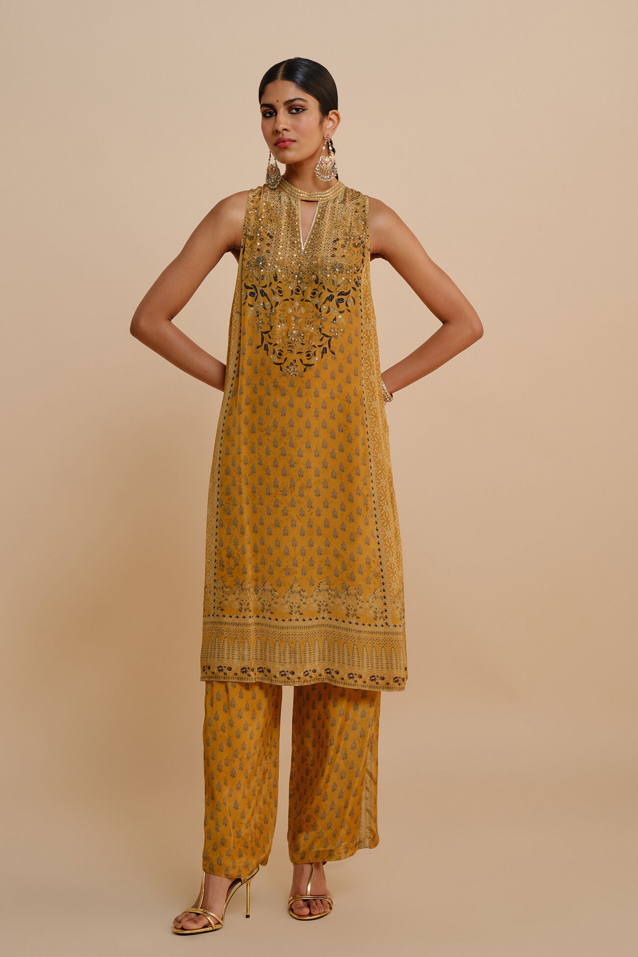 Woman wearing a mustard yellow traditional outfit with intricate designs on a beige background