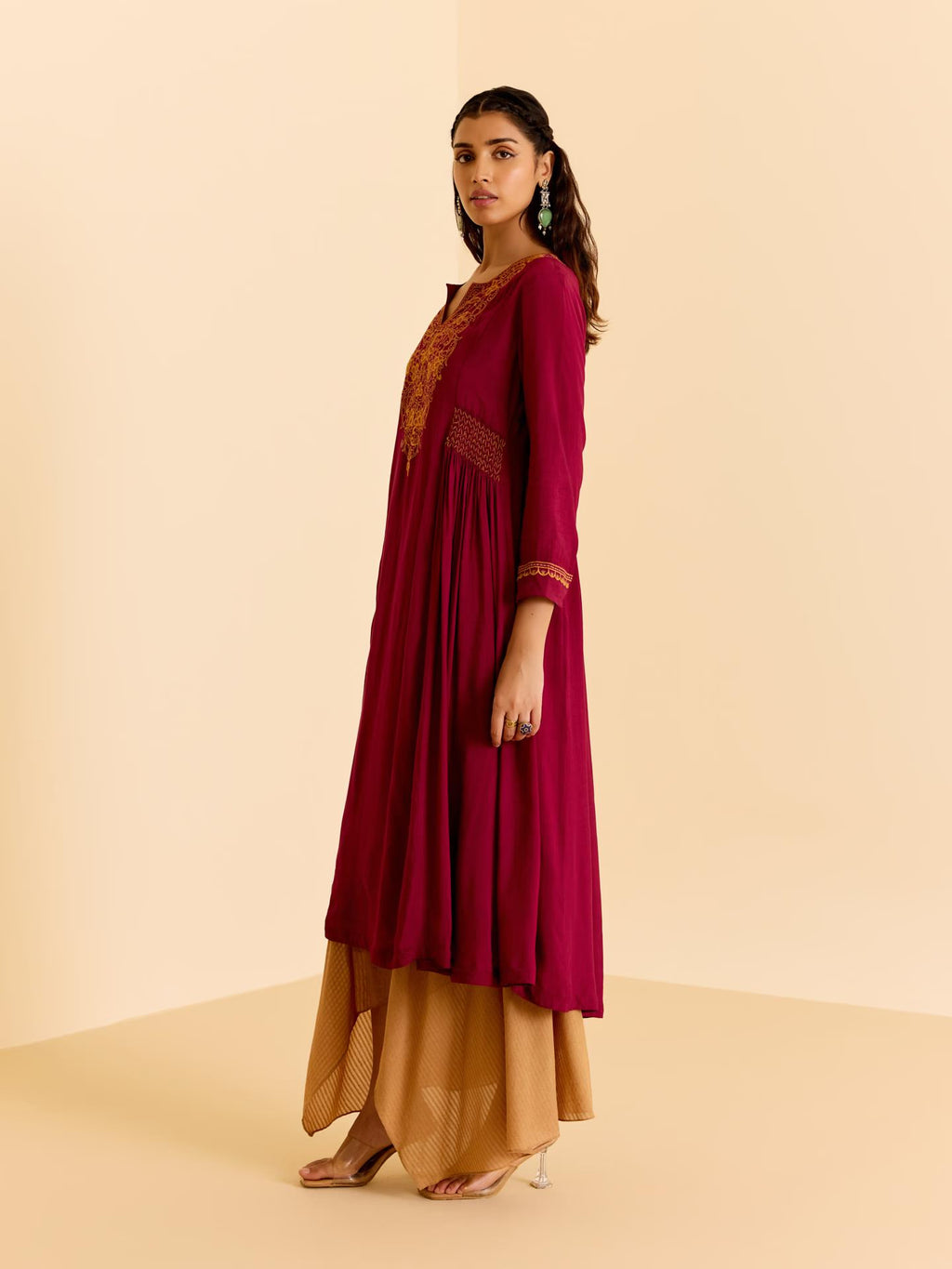 Woman wearing a maroon and gold traditional outfit on a beige background