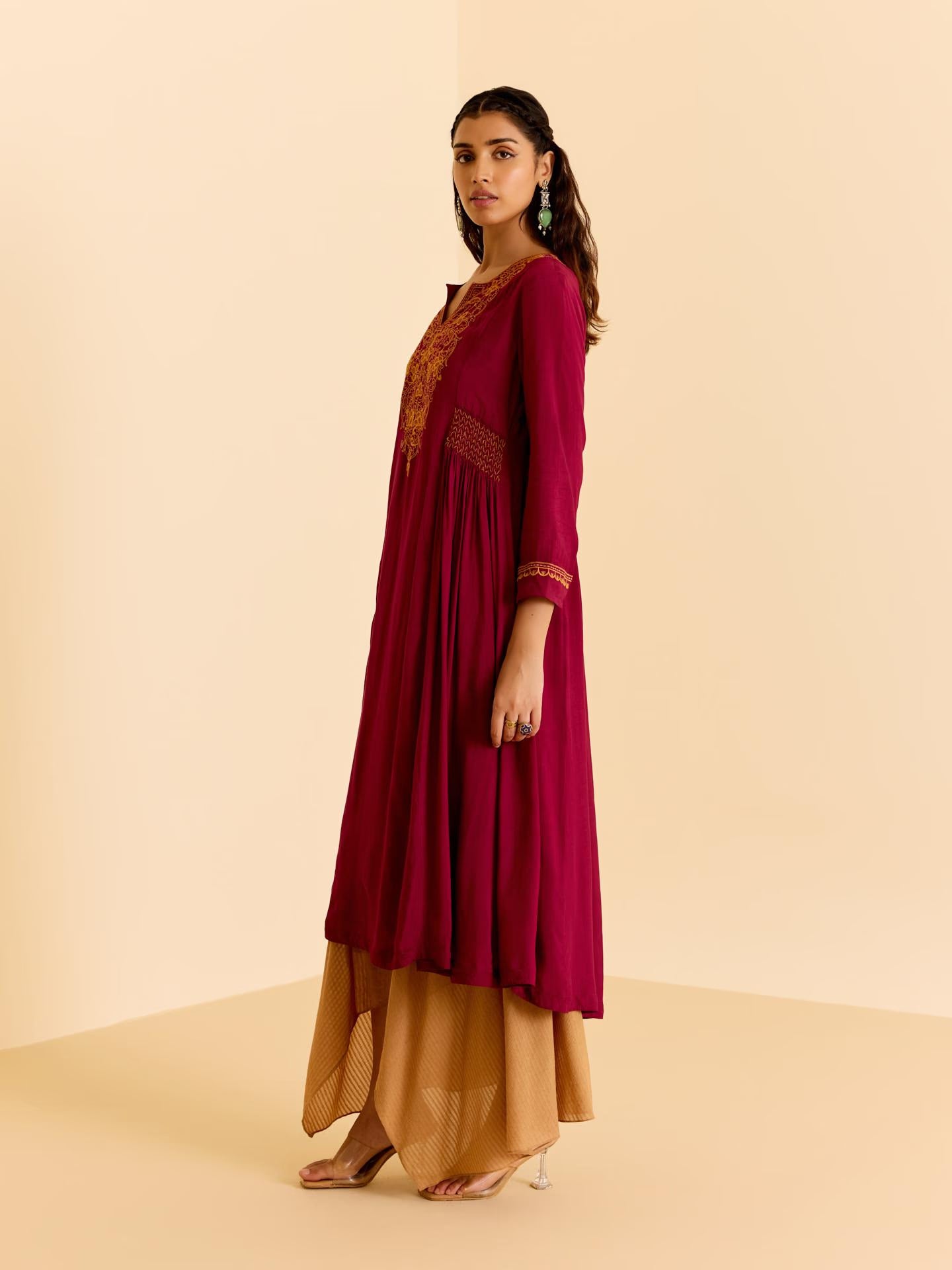 Woman wearing a maroon and gold traditional outfit on a beige background