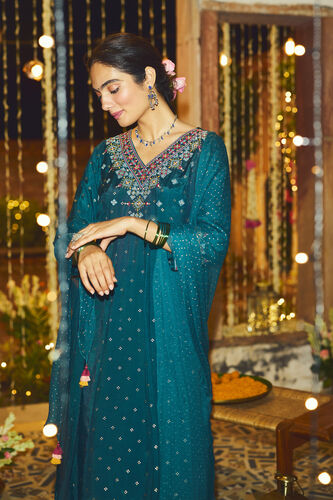 Woman in a teal embroidered outfit with floral decorations in a festive setting