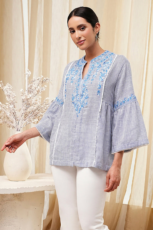 Woman wearing a blue and white striped blouse with floral embroidery in a neutral setting.