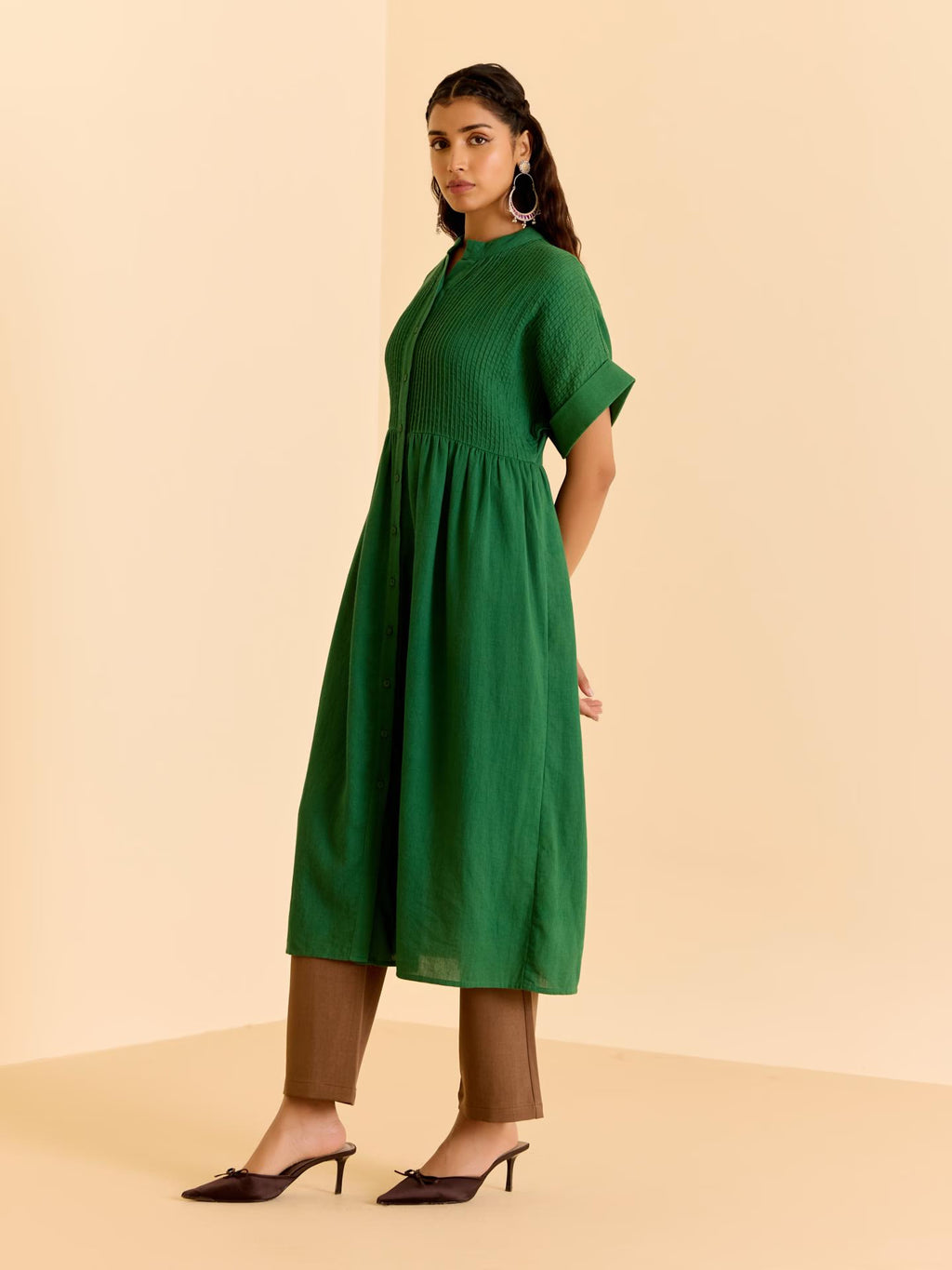 Woman wearing a green dress and brown pants on a beige background