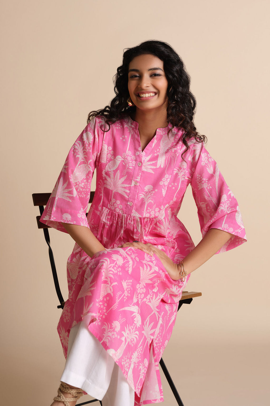 Woman wearing a pink floral dress sitting on a chair against a beige background