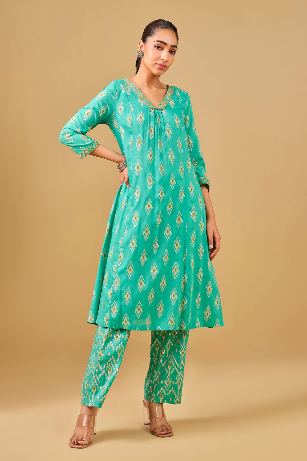Woman wearing a green patterned kurta with matching pants on a beige background