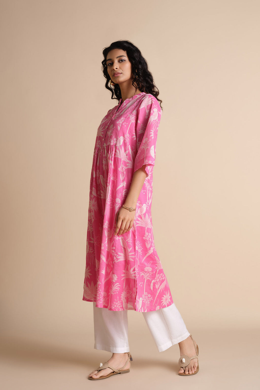 Woman wearing a pink kurta with white pants on a beige background