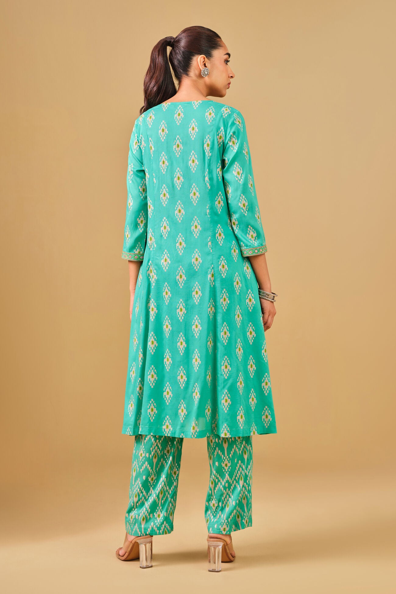 Woman wearing a green patterned kurta with pants on a beige background