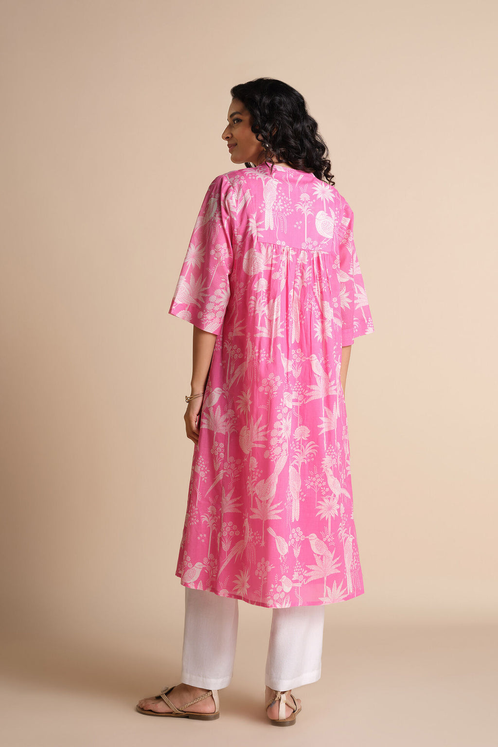 Woman wearing a pink floral kurta with white pants on a beige background