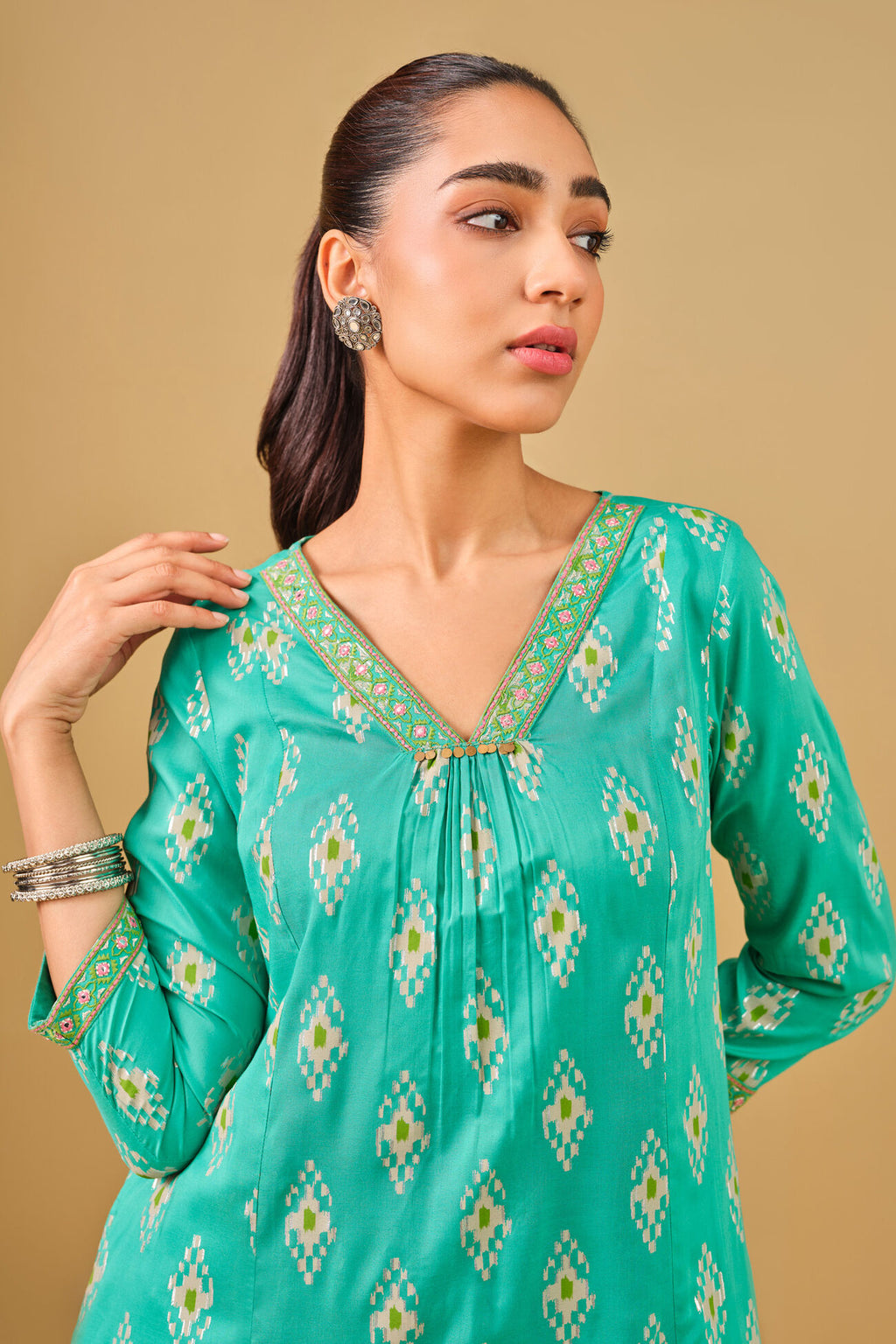 Woman wearing a green patterned kurta against a beige background
