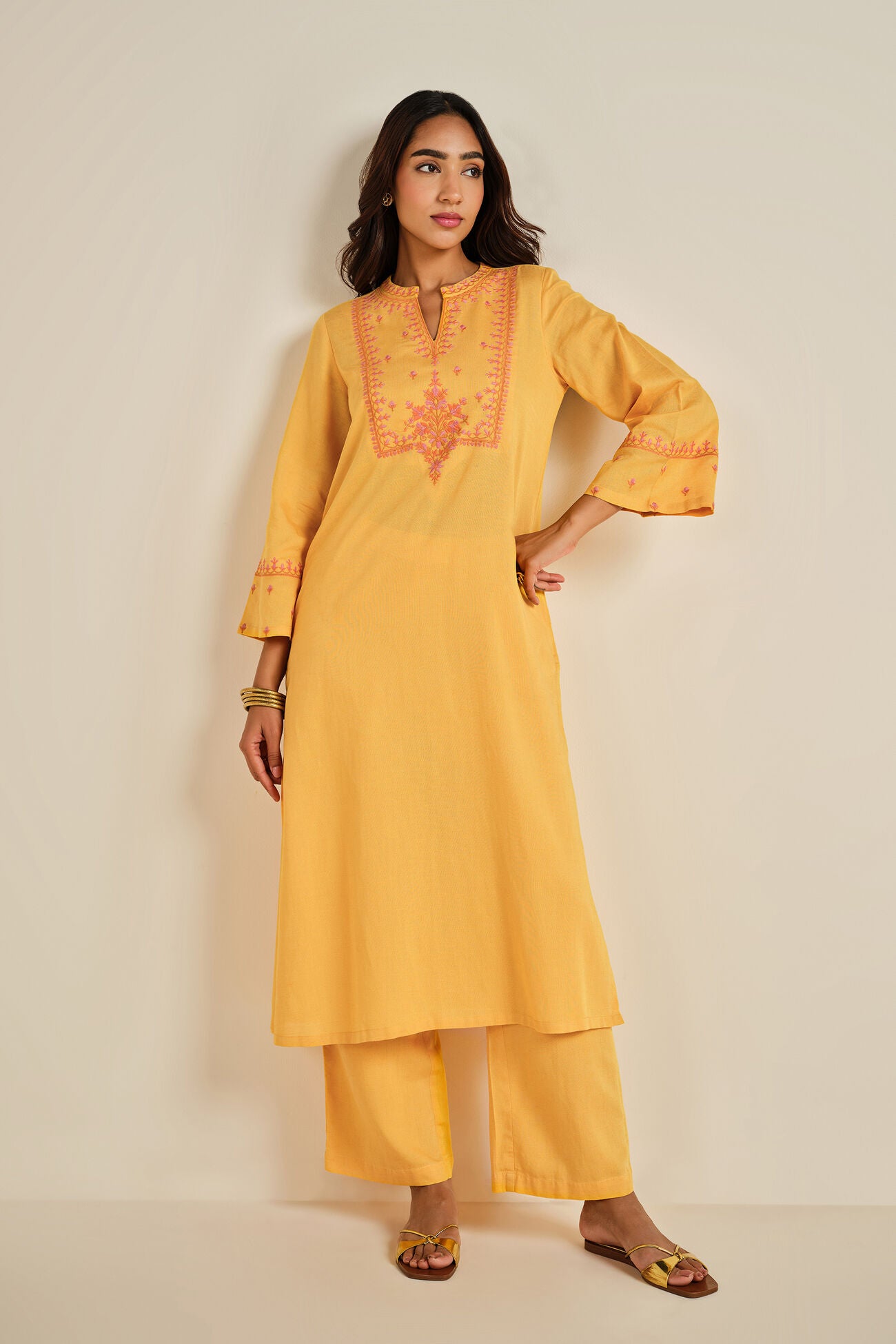 Woman wearing a yellow kurta with intricate embroidery on a beige background