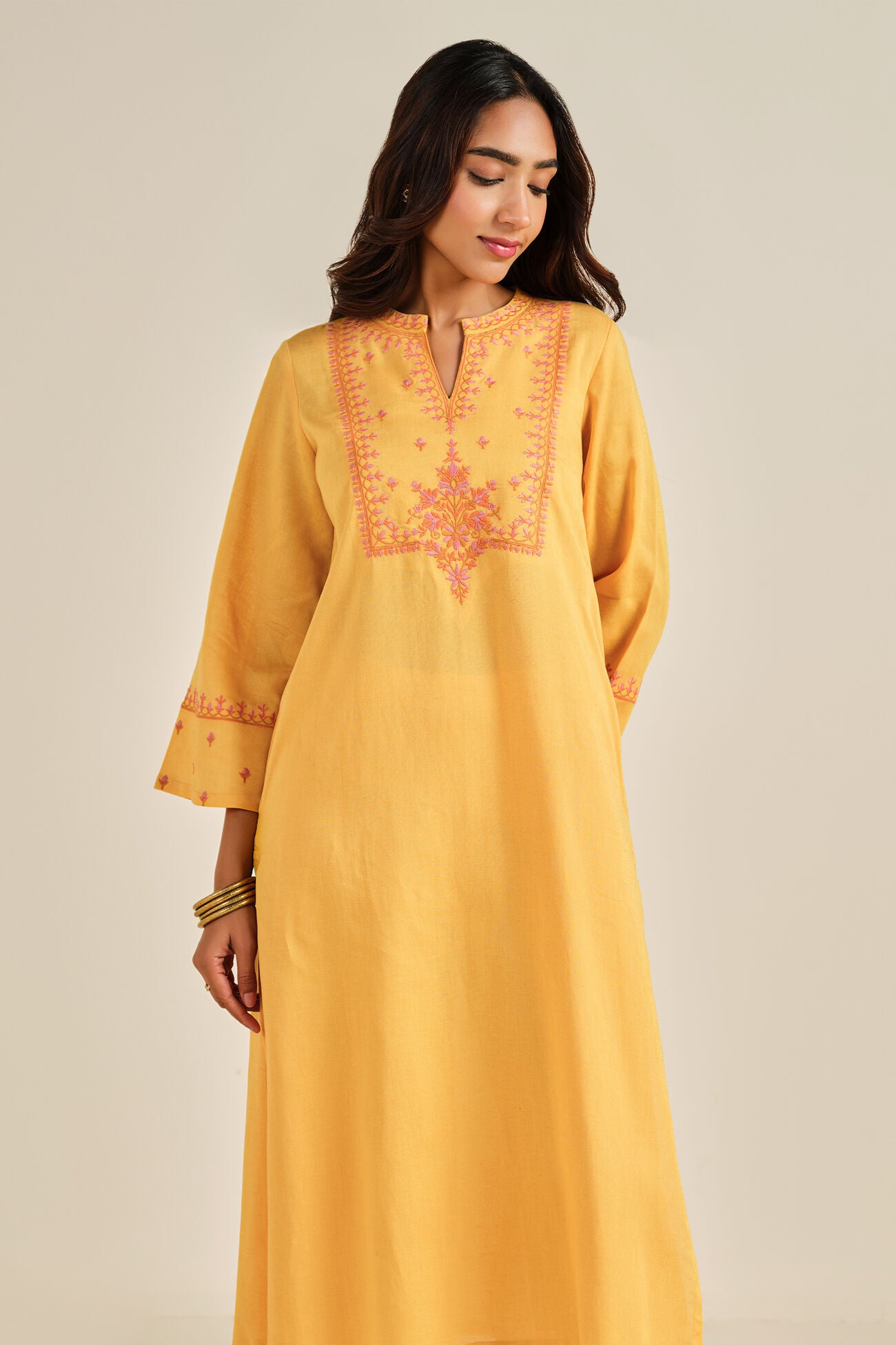 Woman wearing a yellow kurta with intricate embroidery on a beige background