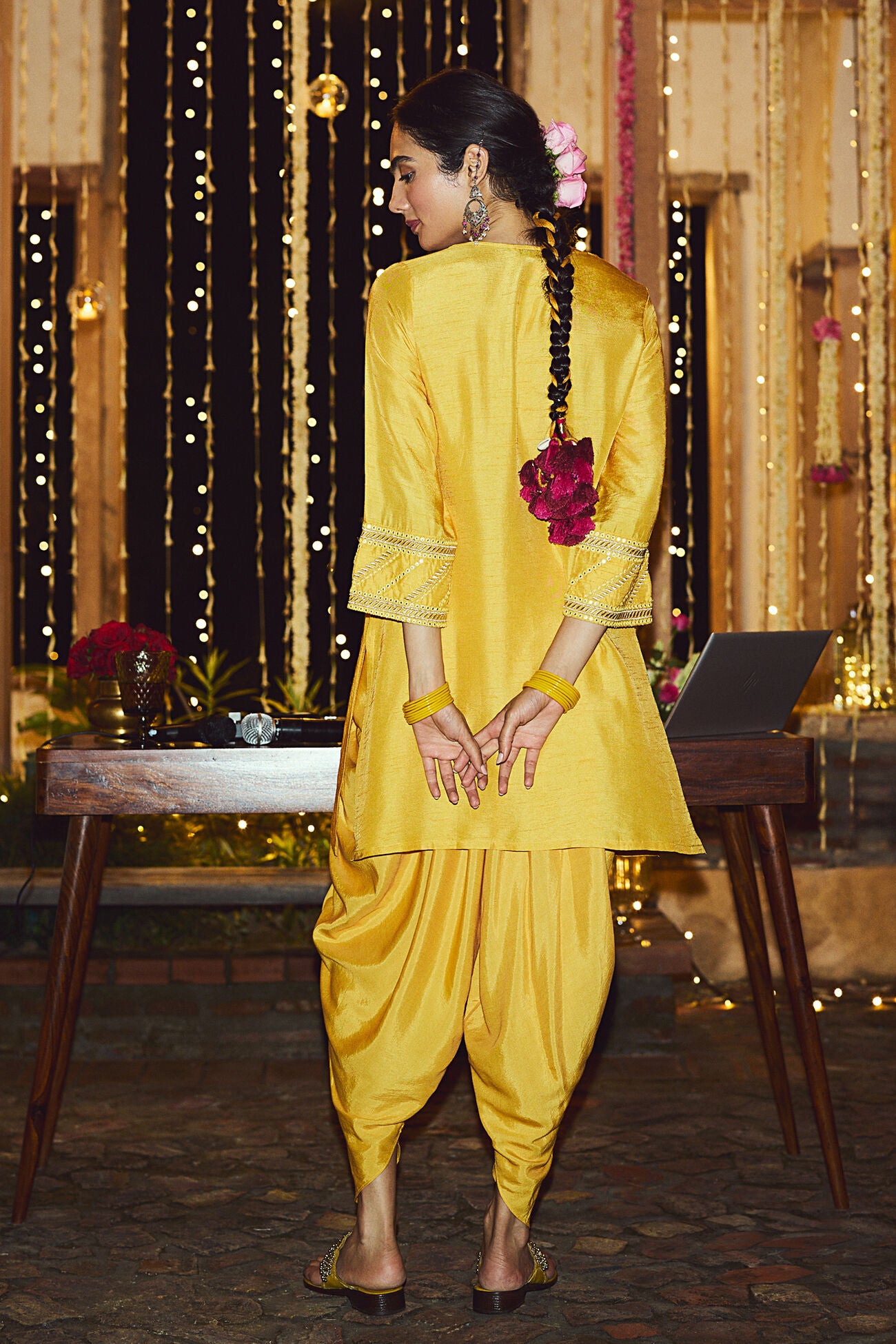 Woman in a yellow traditional outfit standing in front of decorative lights.