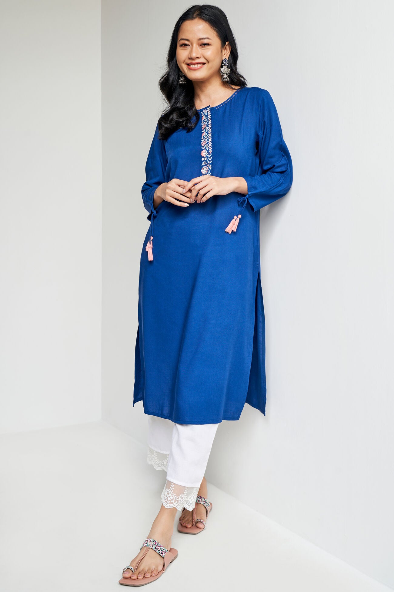 Woman wearing a blue kurta with white pants against a plain background
