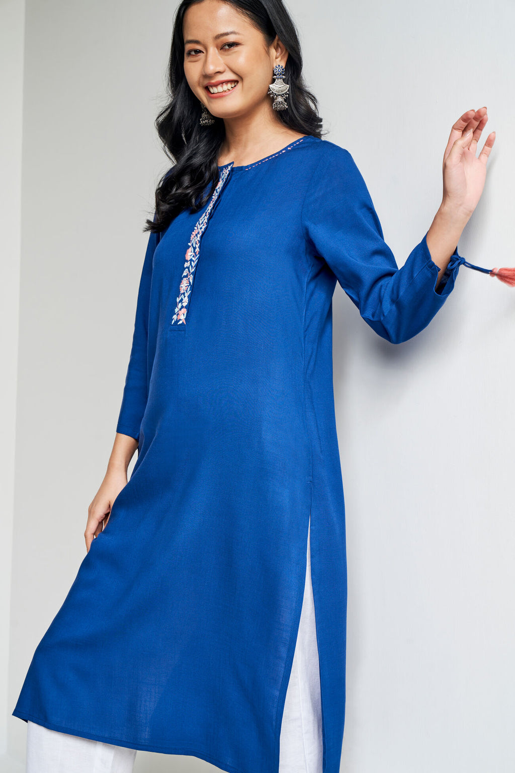 Woman wearing a blue kurta with white embroidery on a plain background