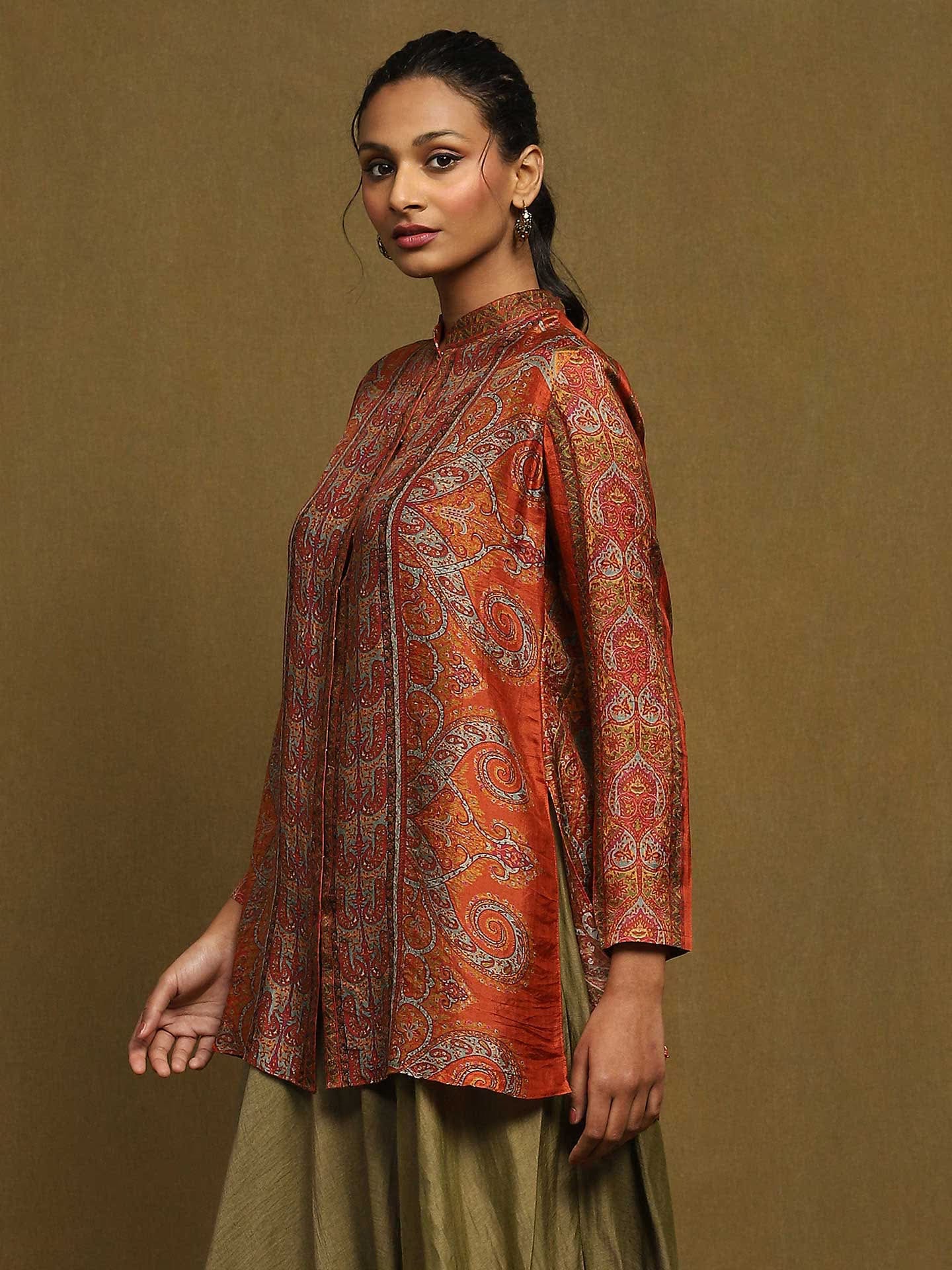 Woman wearing a patterned orange and red top with a plain background