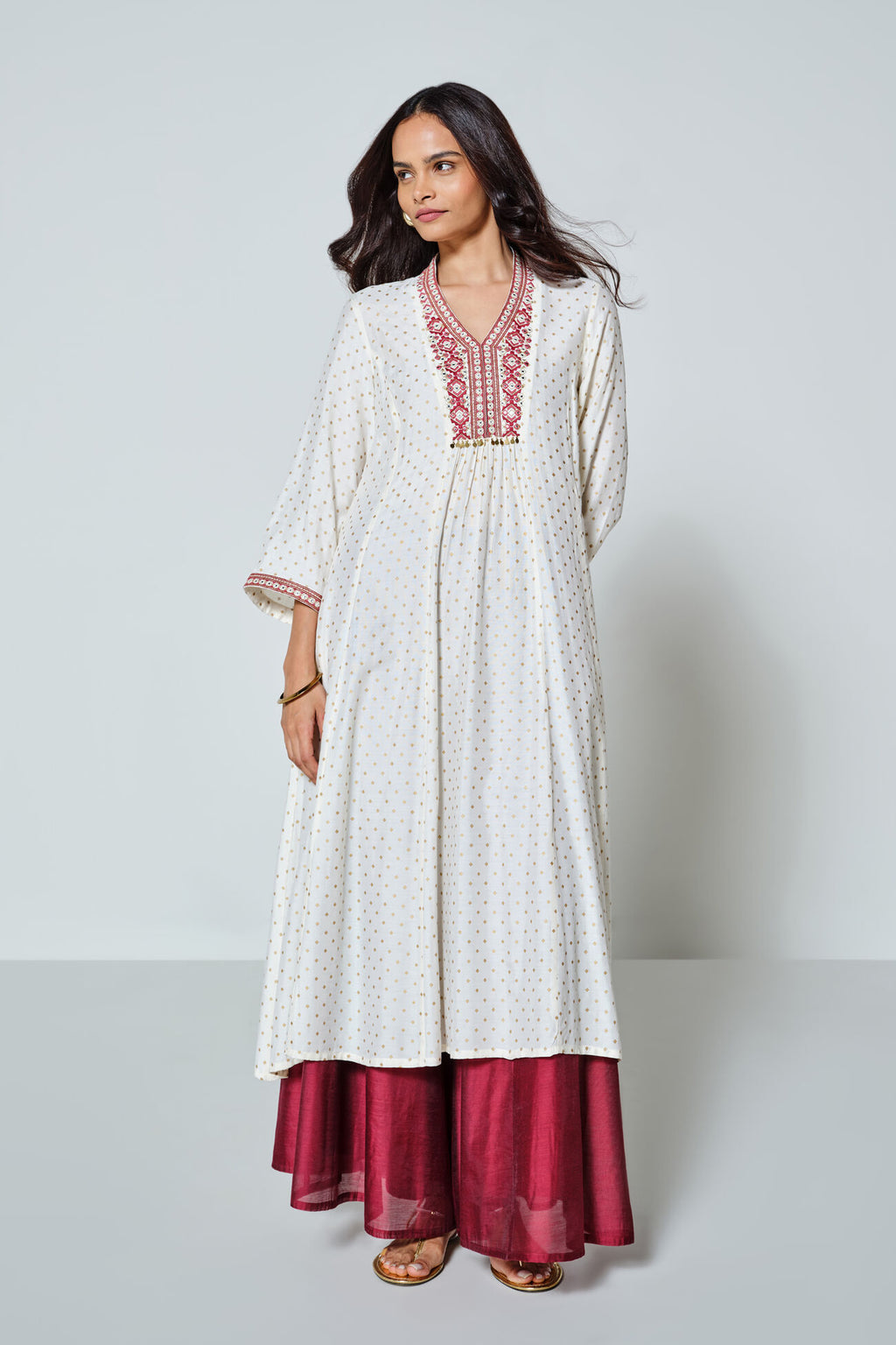 Woman wearing a white embroidered dress with red bottom hem on a light gray background