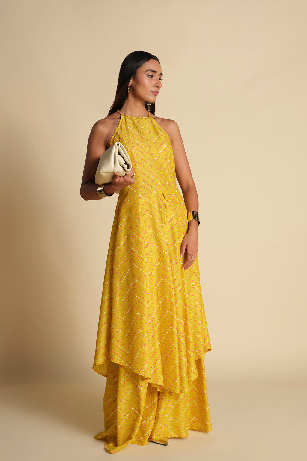Woman wearing a yellow dress holding a clutch against a beige background
