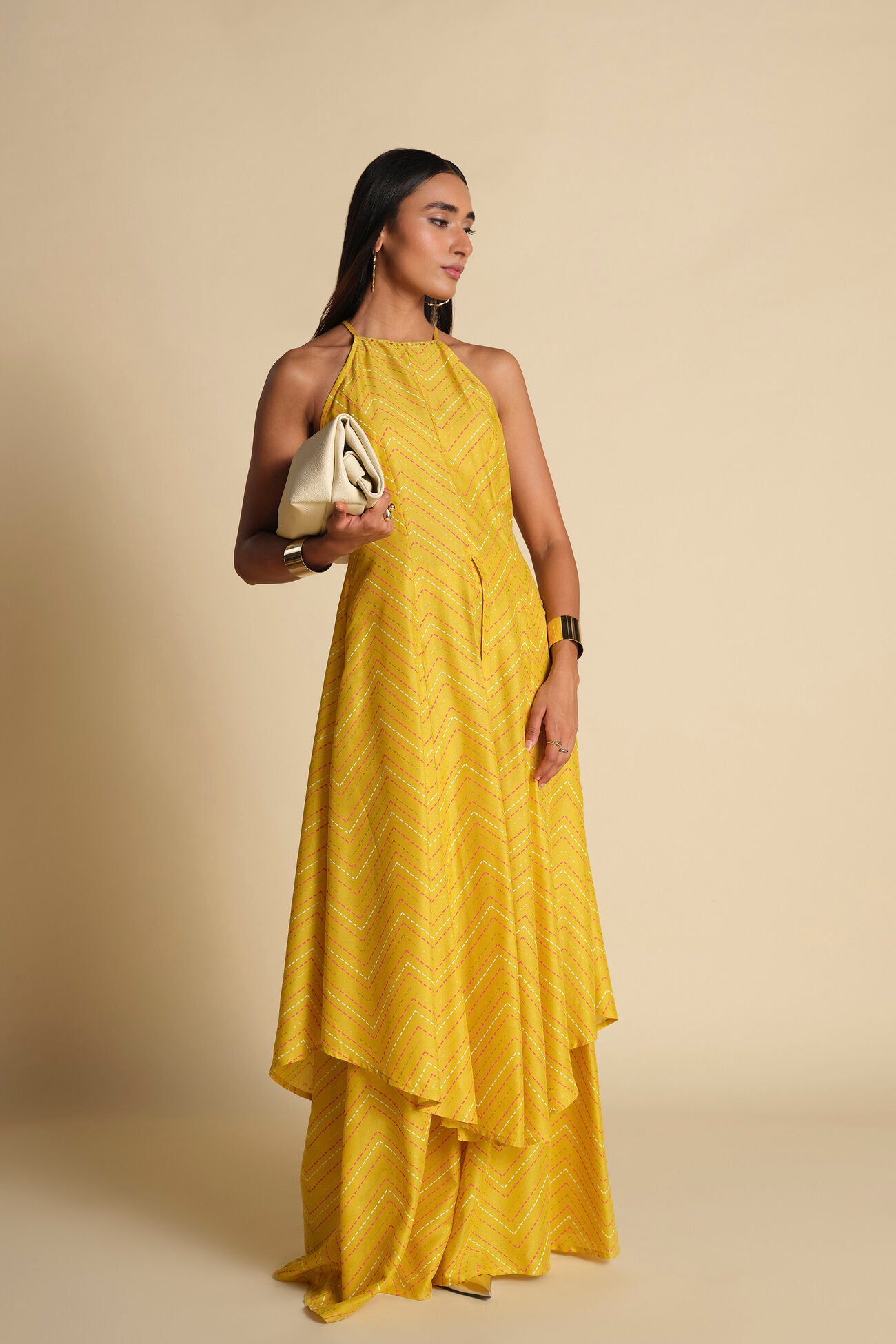 Woman wearing a yellow dress holding a clutch against a beige background