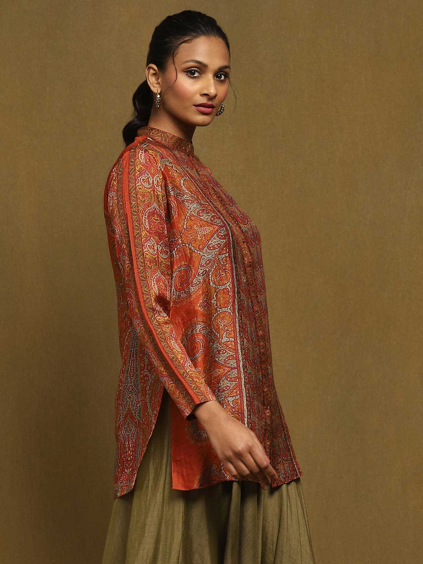 Woman wearing a patterned orange and red top against a beige background