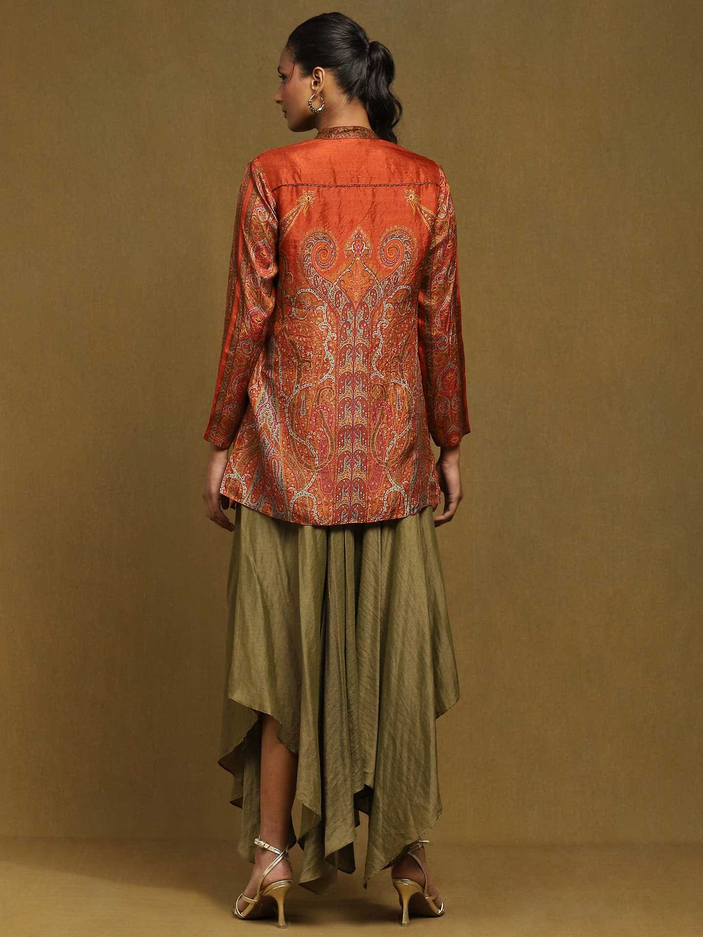 Woman wearing an orange patterned top and green skirt against a brown background