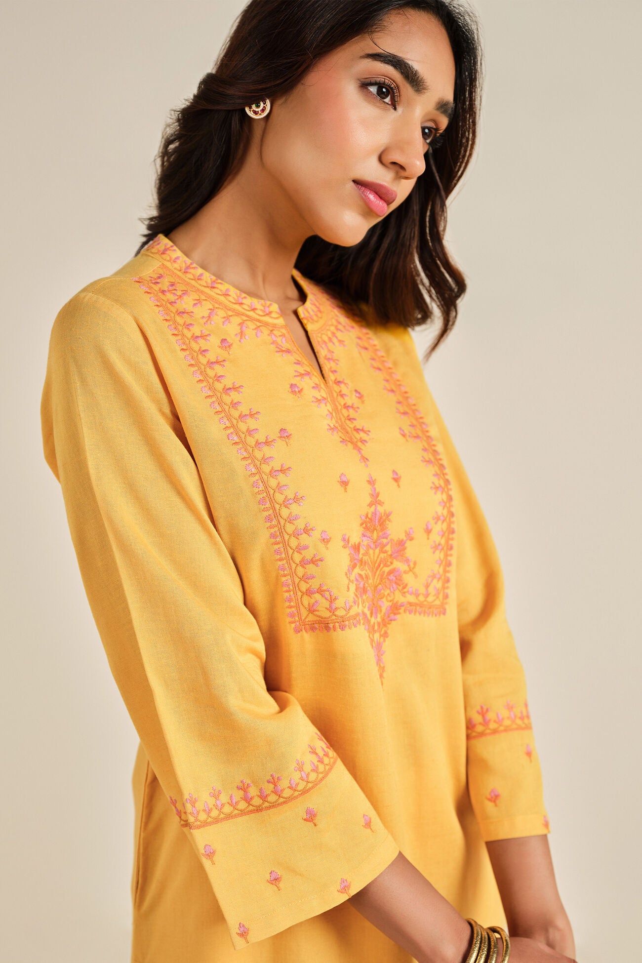 Woman wearing a yellow embroidered kurta against a neutral background