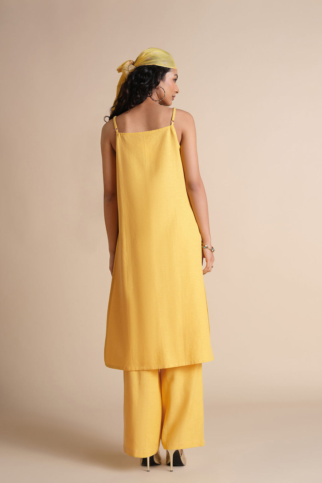 Woman wearing a yellow dress and headscarf against a beige background