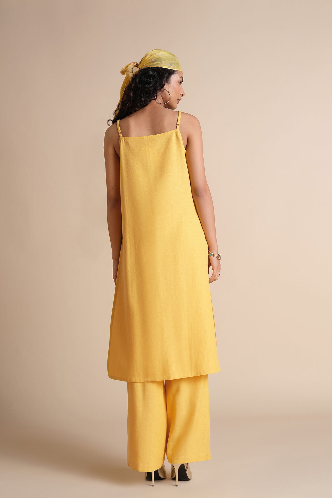 Woman wearing a yellow dress and headscarf against a beige background