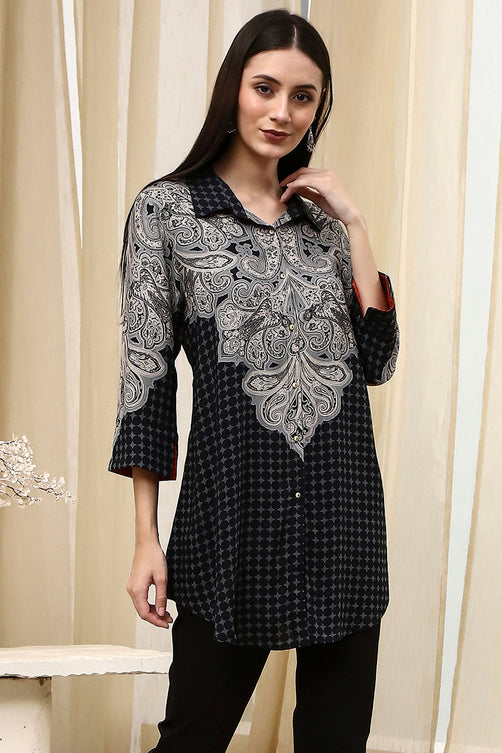 Woman wearing a black and gray patterned top against a beige curtain background