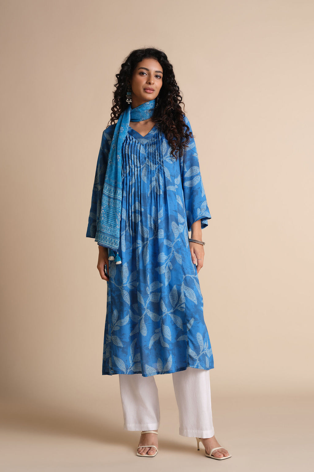 Woman wearing a blue patterned kurta with white pants against a beige background