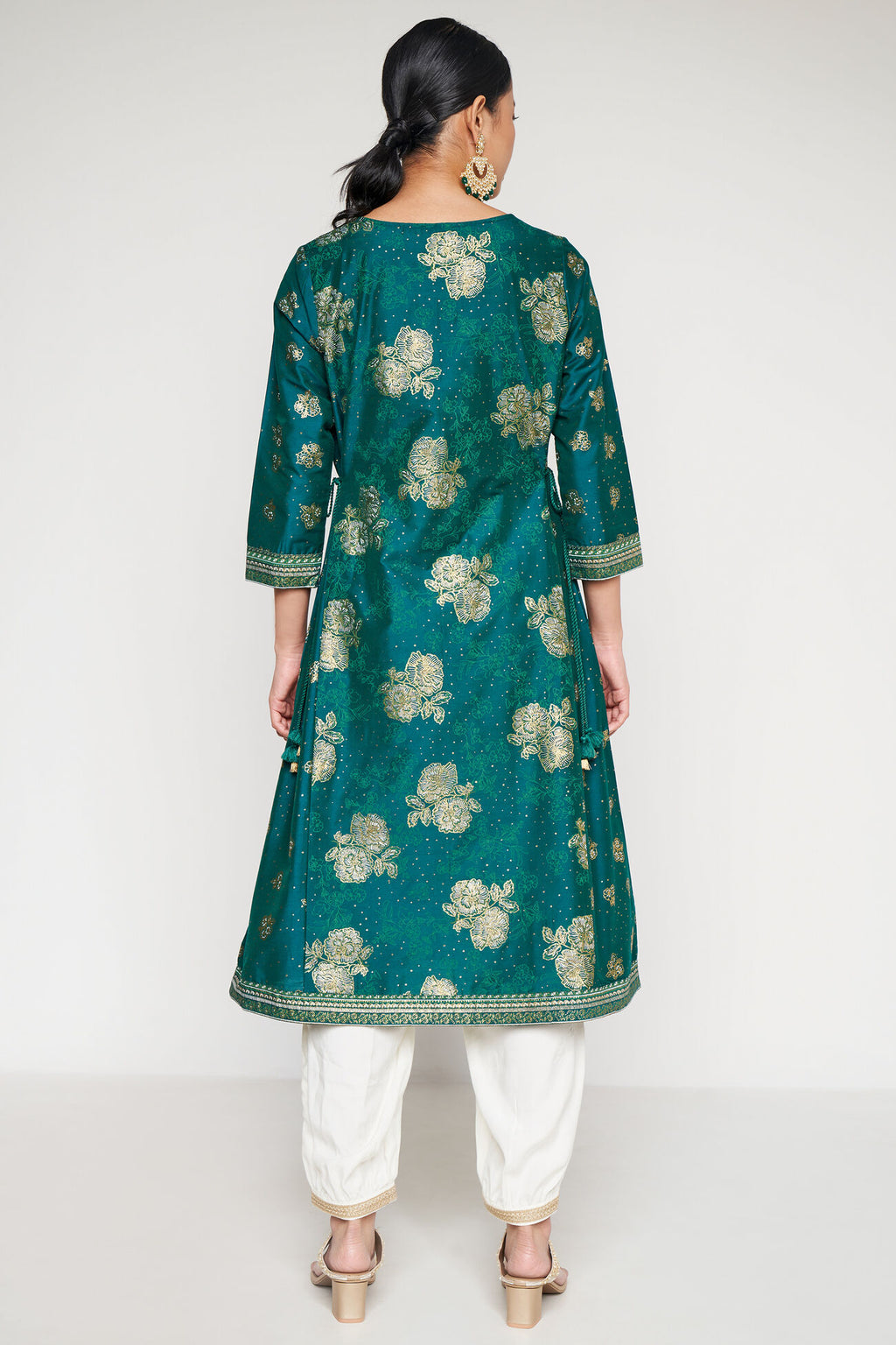Woman wearing a green floral patterned kurta with white pants on a light gray background
